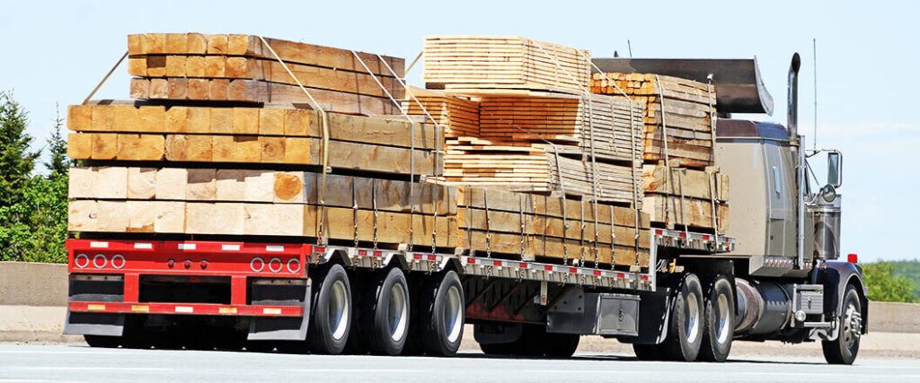 Ein beladener Lkw transportiert schwere Holzbaustoffe auf der Straße.