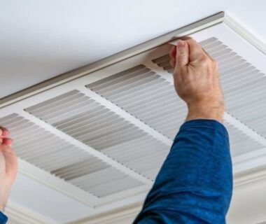 Hände öffnen eine rechteckige Lüftungsabdeckung an der Decke