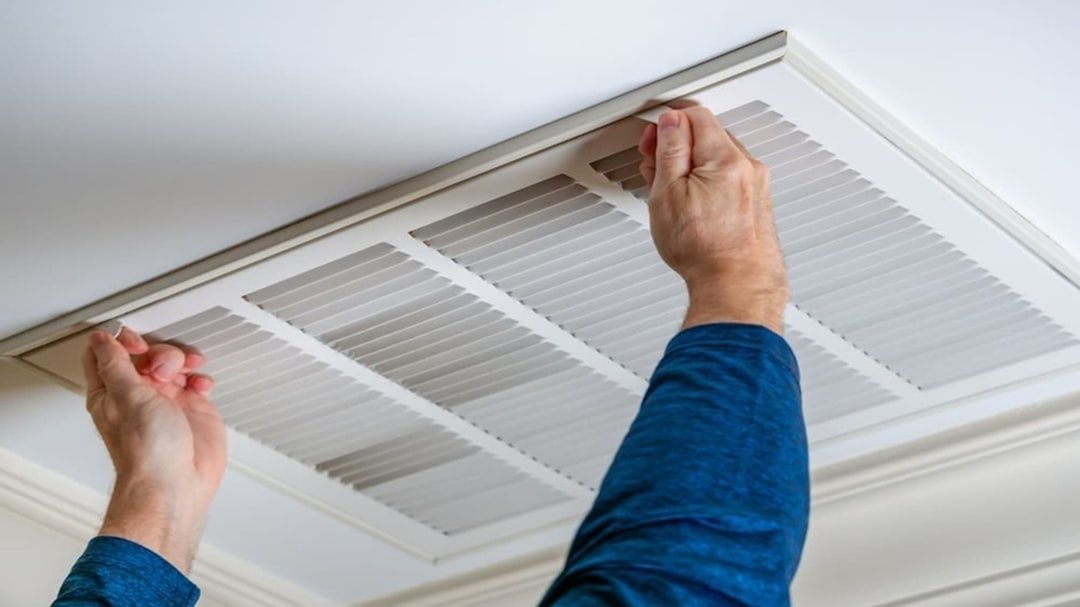 Hände öffnen eine rechteckige Lüftungsabdeckung an der Decke
