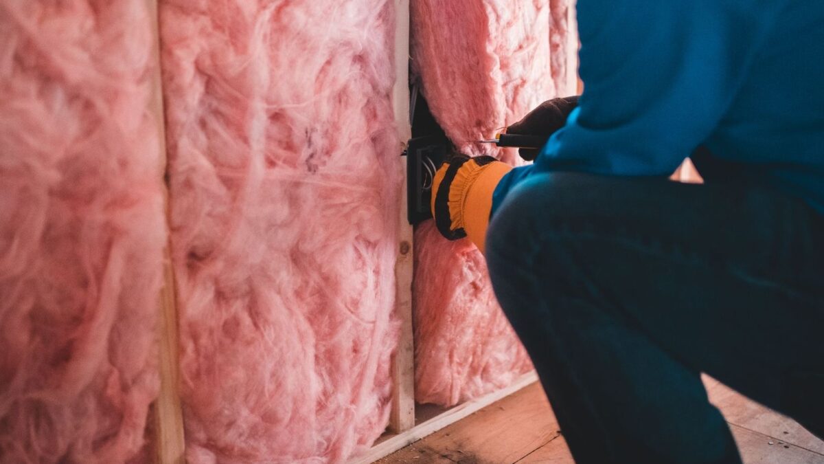Handwerker bringt Dämmstoff zwischen Holzbalken im Dachausbau an