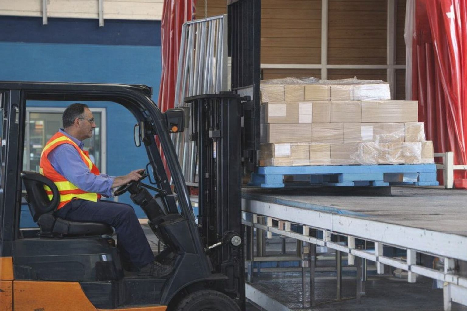 Ein Gabelstaplerfahrer verlädt Paletten mit Baumaterialien in einem Logistikzentrum.